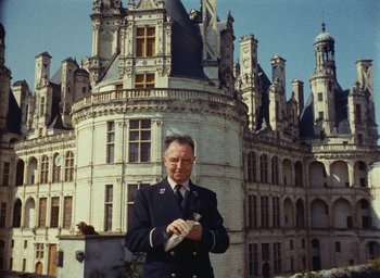 Movie still from “Ô saisons ô chateaux” (1958), directed by Agnès Varda – An older man in a uniform standing in front of a castle; Medium shot, High angle