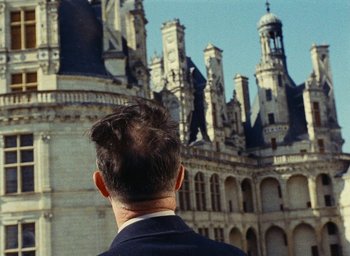 Movie still from “Ô saisons ô chateaux” (1958), directed by Agnès Varda – A man standing in front of an old building; Medium shot, High angle