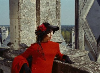 Movie still from “Ô saisons ô chateaux” (1958), directed by Agnès Varda – A woman in a red dress wearing a hat and black gloves; Medium shot, High angle