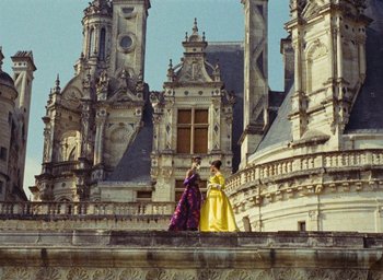 Movie still from “Ô saisons ô chateaux” (1958), directed by Agnès Varda – Two women in long dresses standing on a stone wall; Extreme Wide shot, High angle