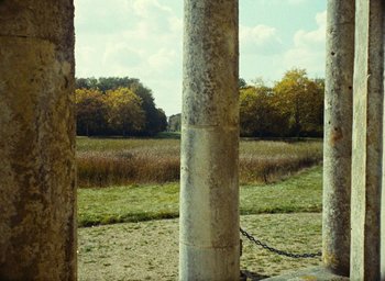 Movie still from “Ô saisons ô chateaux” (1958), directed by Agnès Varda – A view of a grassy field from behind two pillars; Extreme Wide shot, Low angle