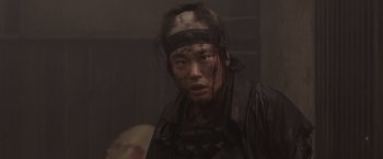 Movie still from “13 Assassins” (2010), directed by Takashi Miike – A person with a blood covered face and a knife in his hand; Close Up shot, Over the shoulder angle
