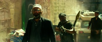 Movie still from “13 Hours” (2016), directed by Michael Bay – A man in a black jacket and a man in a white hat; Medium shot, Low angle