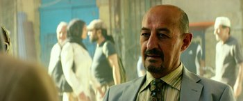 Movie still from “13 Hours” (2016), directed by Michael Bay – A man in a suit and tie standing in front of a group of people; Close Up shot, Over the shoulder angle