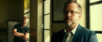 Movie still from “13 Hours” (2016), directed by Michael Bay – A person wearing glasses and a suit; Close Up shot, Low angle