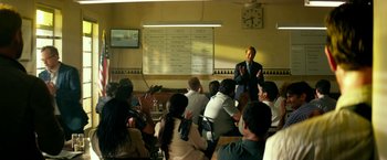 Movie still from “13 Hours” (2016), directed by Michael Bay – A group of people sitting in front of a man in a suit; Wide shot, Over the shoulder angle