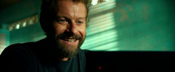 Movie still from “13 Hours” (2016), directed by Michael Bay – A person with a beard smiling; Close Up shot, Over the shoulder angle