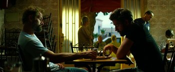 Movie still from “13 Hours” (2016), directed by Michael Bay – Two people sitting at a table with a plate of food in front of them; Medium shot, Low angle