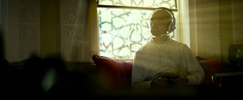 Movie still from “13 Hours” (2016), directed by Michael Bay – A man sitting on a couch wearing a headset and holding a remote; Close Up shot, Over the shoulder angle