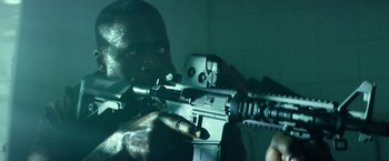 Movie still from “13 Hours” (2016), directed by Michael Bay – A man holding an automatic rifle in a room; Close Up shot, Low angle