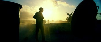 Movie still from “13 Hours” (2016), directed by Michael Bay – A man standing on a street in front of a sunset; Wide shot, Low angle
