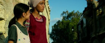 Movie still from “13 Hours” (2016), directed by Michael Bay – A young girl wearing a head scarf is standing in front of a building; Medium shot, Low angle