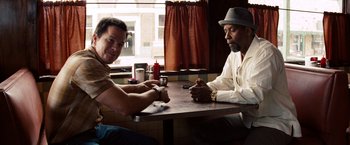 Movie still from “2 Guns” (2013), directed by Baltasar Kormákur – Two men sitting at a table in front of a window; Medium shot, Over the shoulder angle