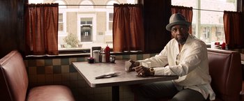 Movie still from “2 Guns” (2013), directed by Baltasar Kormákur – A man sitting at a table in front of an open window; Medium shot, Over the shoulder angle