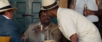 Movie still from “2 Guns” (2013), directed by Baltasar Kormákur – A man wearing a hat and a suit is talking to another man in front of a bottle; Medium shot, Over the shoulder angle
