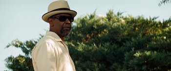 Movie still from “2 Guns” (2013), directed by Baltasar Kormákur – A man wearing a hat and sunglasses standing in front of trees; Close Up shot, Low angle