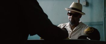 Movie still from “2 Guns” (2013), directed by Baltasar Kormákur – An older man wearing a hat and sunglasses is sitting at a table; Close Up shot, Over the shoulder angle