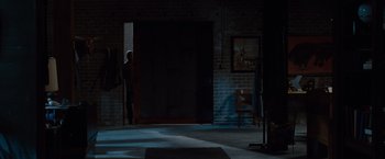 Movie still from “2 Guns” (2013), directed by Baltasar Kormákur – A man standing in a dark room next to an open door; Wide shot, Over the shoulder angle