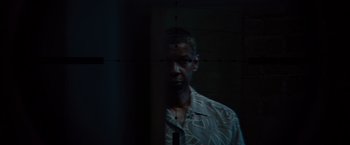 Movie still from “2 Guns” (2013), directed by Baltasar Kormákur – A man standing in a dark room looking at the camera; Close Up shot, Over the shoulder angle