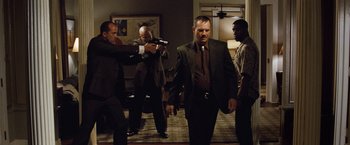 Movie still from “2 Guns” (2013), directed by Baltasar Kormákur – A group of men standing around a room with a gun; Wide shot, Low angle