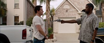 Movie still from “2 Guns” (2013), directed by Baltasar Kormákur – A man holding a gun pointed at another man in front of a house; Medium shot, Over the shoulder angle