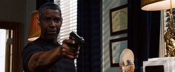 Movie still from “2 Guns” (2013), directed by Baltasar Kormákur – A man holding a gun in a room; Medium shot, Over the shoulder angle