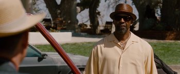 Movie still from “2 Guns” (2013), directed by Baltasar Kormákur – A man wearing a hat and sunglasses standing next to a tree; Medium shot, Over the shoulder angle