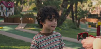 Movie still from “20th Century Women” (2016), directed by Mike Mills – A young boy is smiling while standing in a park; Close Up shot, Over the shoulder angle