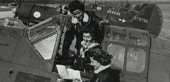 Movie still from “20th Century Women” (2016), directed by Mike Mills – A group of women are looking at a map in an airplane cockpit; Medium shot, Low angle