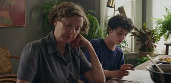 Movie still from “20th Century Women” (2016), directed by Mike Mills – A woman sitting next to a boy at a table; Medium shot, Over the shoulder angle