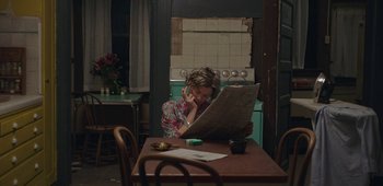 Movie still from “20th Century Women” (2016), directed by Mike Mills – A woman sitting at a table reading a newspaper; Medium shot, High angle