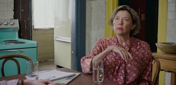 Movie still from “20th Century Women” (2016), directed by Mike Mills – A woman sitting at a table in front of a glass of water; Close Up shot, Over the shoulder angle