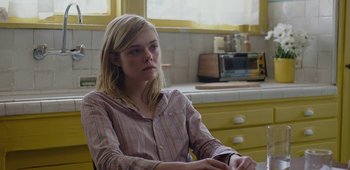 Movie still from “20th Century Women” (2016), directed by Mike Mills – A woman sitting in a chair in front of a microwave; Medium shot, Over the shoulder angle