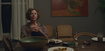 Movie still from “20th Century Women” (2016), directed by Mike Mills – A woman sitting at a table in front of plates of food; Medium shot, Over the shoulder angle