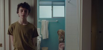 Movie still from “20th Century Women” (2016), directed by Mike Mills – A young man standing in a bathroom next to a window; Medium shot, Over the shoulder angle