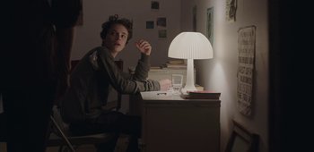 Movie still from “20th Century Women” (2016), directed by Mike Mills – A boy sitting at a desk with a lamp on top of a table; Medium shot, Over the shoulder angle