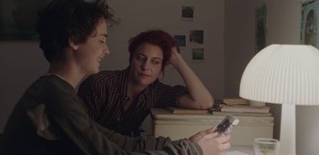 Movie still from “20th Century Women” (2016), directed by Mike Mills – Two people sitting at a table looking at a cell phone; Medium shot, Over the shoulder angle