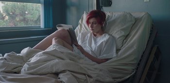 Movie still from “20th Century Women” (2016), directed by Mike Mills – A woman with red hair laying in a bed reading a book; Medium shot, Overhead angle