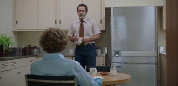 Movie still from “20th Century Women” (2016), directed by Mike Mills – A man standing in front of a table holding a coffee cup; Medium shot, Over the shoulder angle