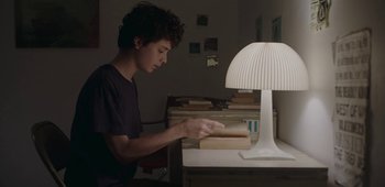 Movie still from “20th Century Women” (2016), directed by Mike Mills – A young man is sitting at a desk by a lamp; Medium shot, High angle