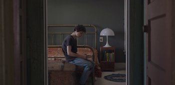 Movie still from “20th Century Women” (2016), directed by Mike Mills – A young man sitting on a bed looking at his cell phone; Medium shot, High angle