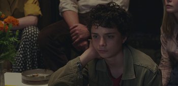 Movie still from “20th Century Women” (2016), directed by Mike Mills – A young man sitting on the ground with his hand on his chin; Close Up shot, Over the shoulder angle