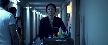 Movie still from “3 Days to Kill” (2014), directed by McG – A woman holding a box of office supplies in a hotel hallway; Medium shot, Low angle