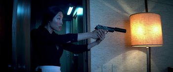 Movie still from “3 Days to Kill” (2014), directed by McG – A woman is holding a gun in a room; Medium shot, Low angle