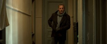 Movie still from “3 Days to Kill” (2014), directed by McG – A man standing in front of a door wearing gloves; Medium shot, Low angle