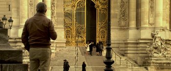 Movie still from “3 Days to Kill” (2014), directed by McG – A group of people standing on steps in front of a building; Wide shot, Over the shoulder angle