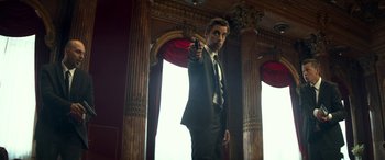 Movie still from “3 Days to Kill” (2014), directed by McG – A man in a suit and tie holding a gun in his hand; Medium shot, Low angle