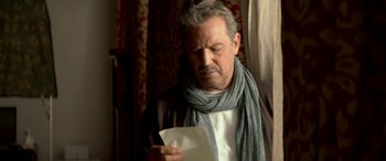 Movie still from “3 Days to Kill” (2014), directed by McG – An older man holding a piece of paper in front of a window; Close Up shot, Low angle