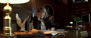 Movie still from “3 Days to Kill” (2014), directed by McG – A woman sitting at a desk talking on a phone; Medium shot, High angle
