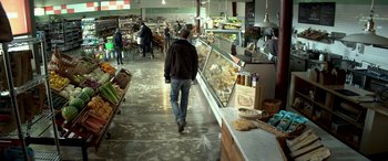 Movie still from “3 Days to Kill” (2014), directed by McG – A man walking through a grocery store filled with food; Wide shot, Over the shoulder angle